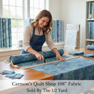 Carmon's Quilt Shop woman cutting denim blue mottled 108 inch wide cotton quilting fabric on a wooden table