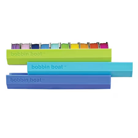 Carmon's Quilt Shop Dritz Bobbin Boat organizers in green, blue, and purple for sewing and quilting storage.