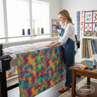 Carmon's Quilt Shop features a woman using a longarm machine with vibrant Fiesta Phantasma hexagon cotton quilt backing.