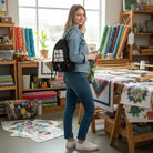 Carmon's Quilt Shop black drawstring backpack with "WE ARE 2022" slogan and colourful polka dots, worn by a woman in a sewing studio.