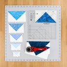Carmon's Quilt Shop Creative Grids Ultimate Flying Geese Tool Two quilting ruler with blue fabric pieces and rotary cutter.