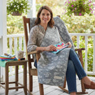 Carmon's Quilt Shop gray 100% cotton fabric with a repeating pattern of airplanes, helicopters, and hot air balloons. A woman sits in a rocking chair holding a small quilt.