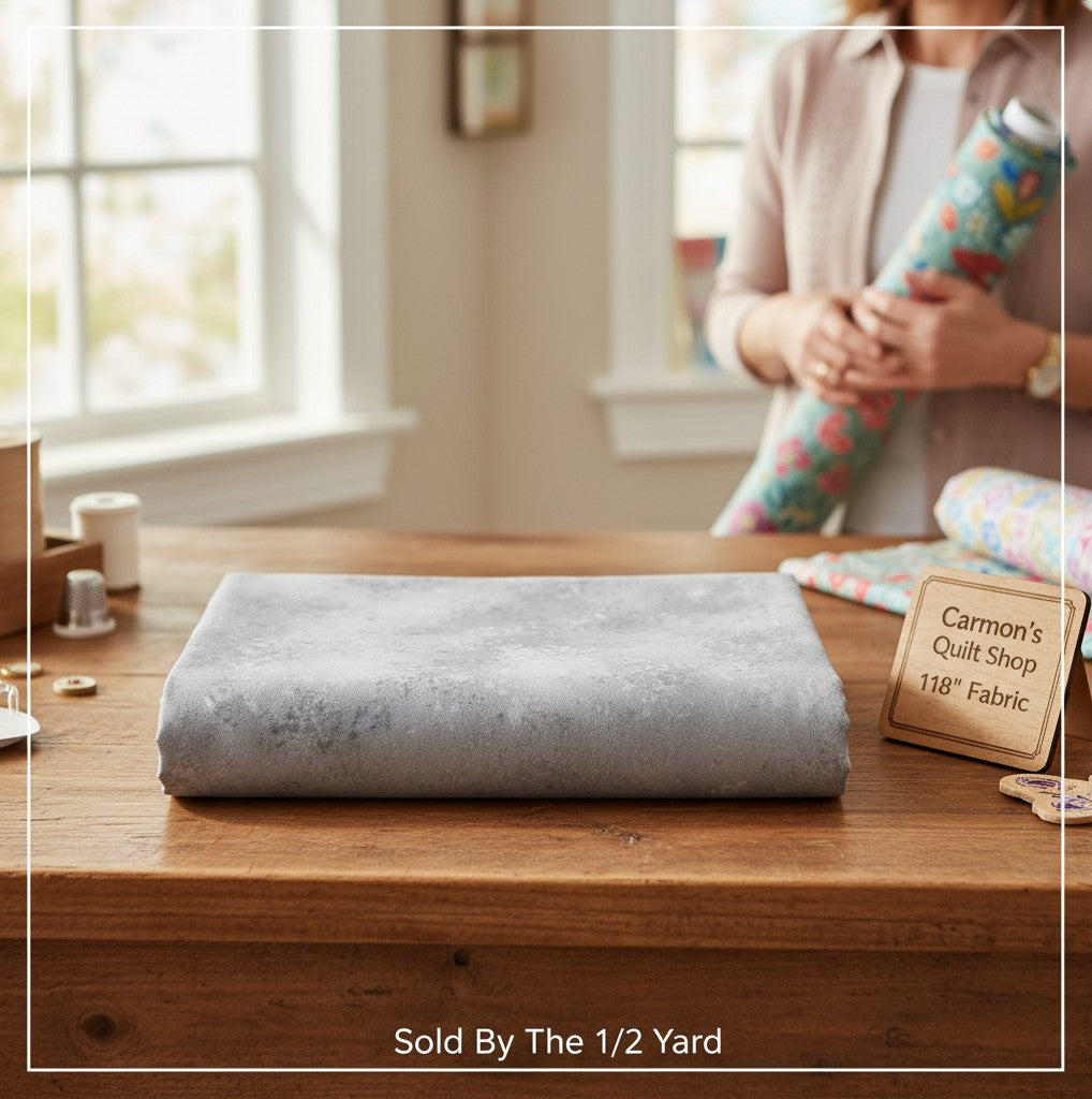 Carmon's Quilt Shop grey mottled Panorama Rapture blender cotton fabric folded on a wooden table for quilting.