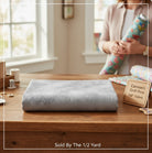 Carmon's Quilt Shop grey mottled Panorama Rapture blender cotton fabric folded on a wooden table for quilting.