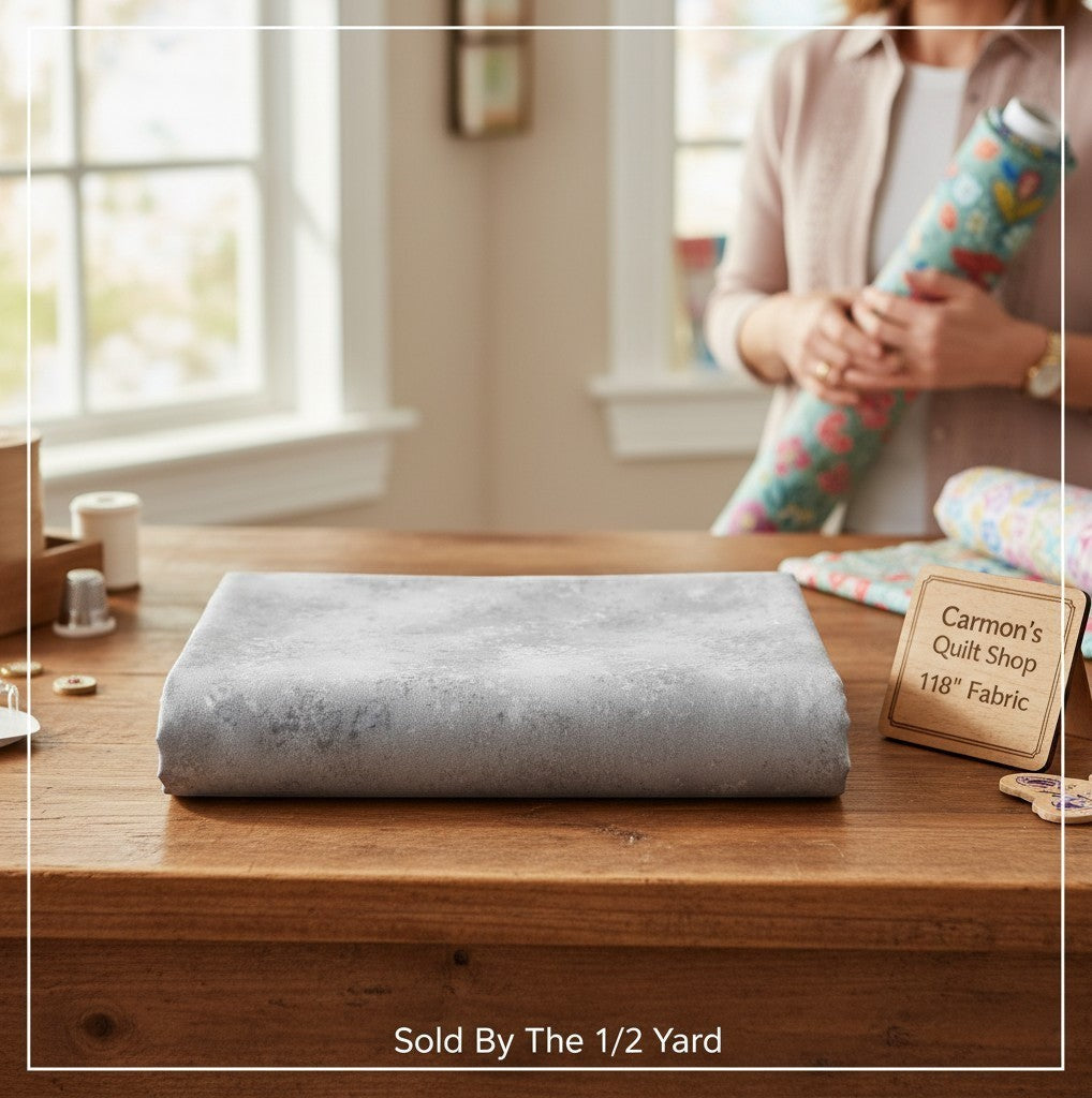 Carmon's Quilt Shop grey mottled Panorama Rapture blender cotton fabric folded on a wooden table for quilting.