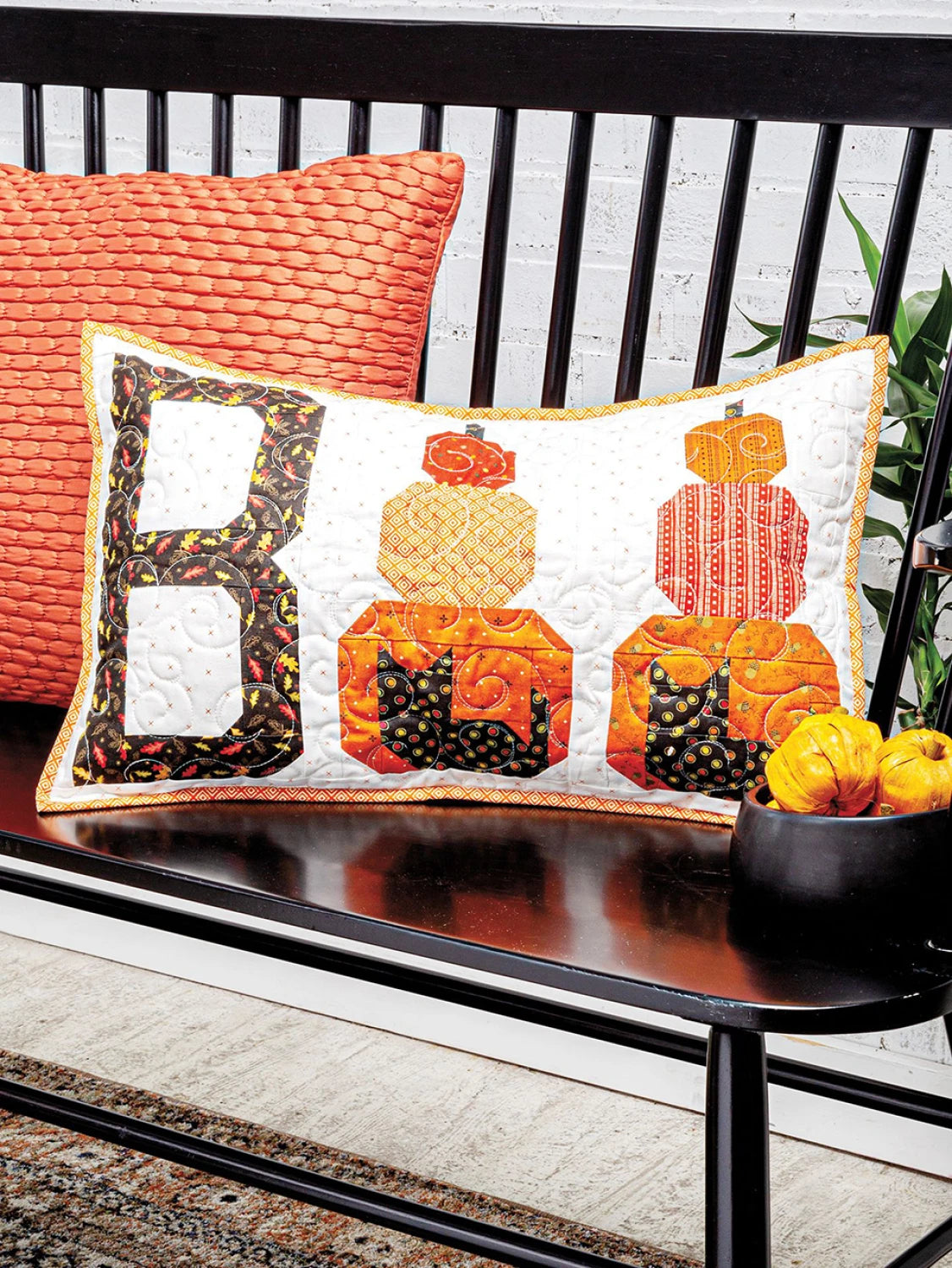 Carmon's Quilt Shop quilted Boo pillow with pumpkin and cat motifs on a black bench for seasonal home decor.