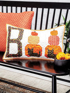 Carmon's Quilt Shop quilted Boo pillow with pumpkin and cat motifs on a black bench for seasonal home decor.