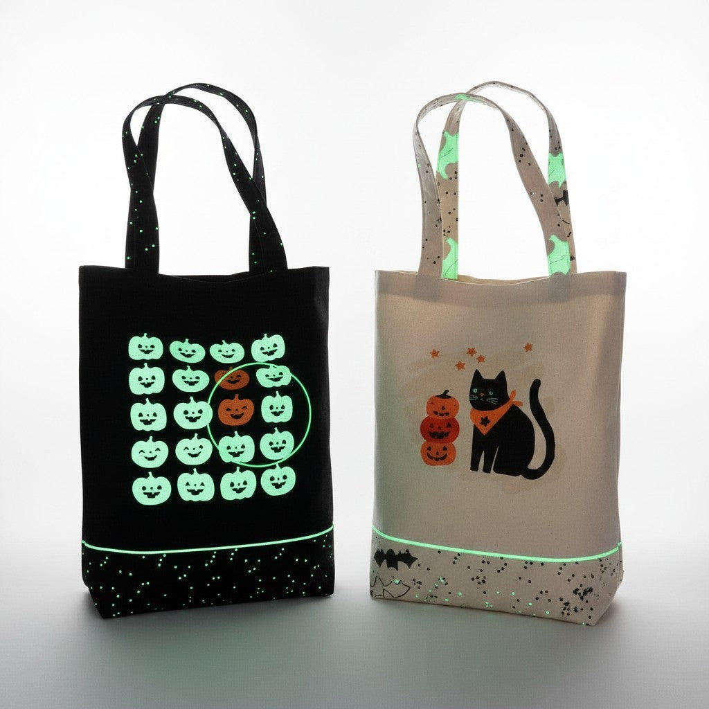Carmon's Quilt Shop Halloween tote bags, one black with glow-in-the-dark pumpkins, one cream with a black cat and pumpkins.