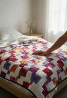Carmon's Quilt Shop LaRue throw quilt featuring a disappearing nine-patch design in purple, orange, and white squares.