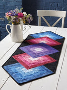 Carmon's Quilt Shop Log Cabin Variations quilt pattern book featuring a colorful geometric table runner project