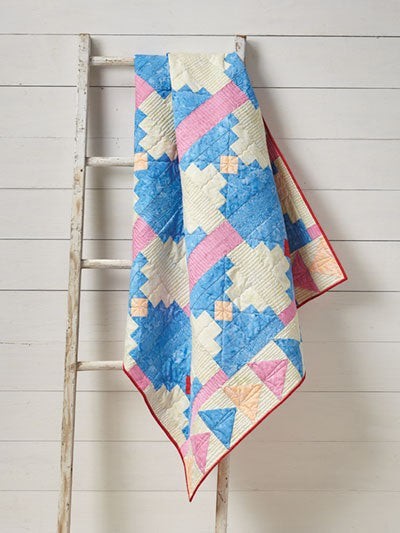 Carmon's Quilt Shop Log Cabin Variations quilt featuring blue, pink, and cream geometric patterns on a wooden ladder.