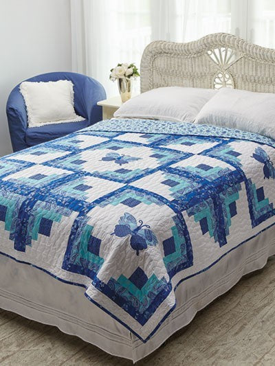 Carmon's Quilt Shop Log Cabin Variations quilt featuring blue and white butterfly patterns on a bed in a bedroom.