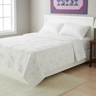 Carmon's Quilt Shop Lovely Flowers quilt pattern featuring soft floral prints on a white bed in a bright bedroom.