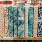 Carmon's Quilt Shop wide backing fabric rolls featuring teal marble and floral patterns on a store shelf.