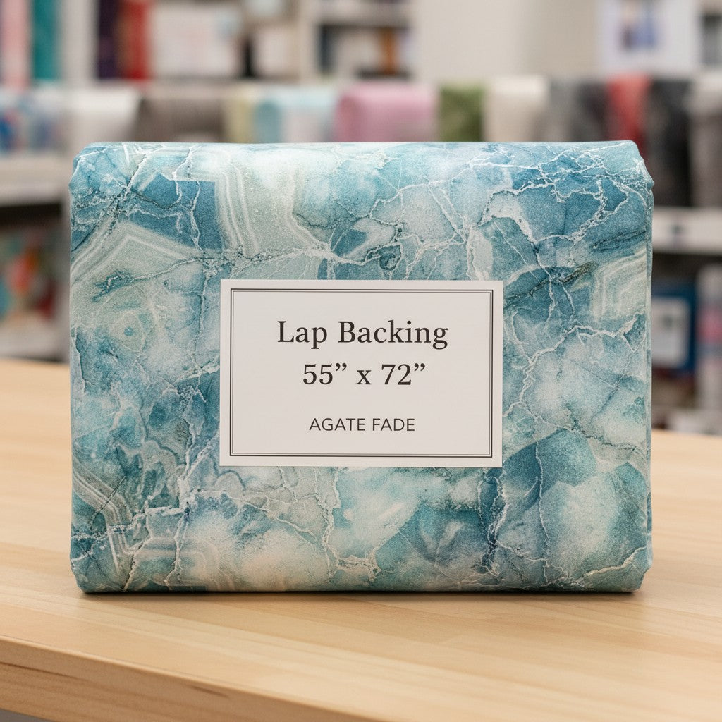 Carmon's Quilt Shop Northcott Smooth Sailing marble pattern quilt backing fabric in teal and white on a wooden table.