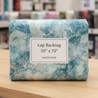 Carmon's Quilt Shop Northcott Smooth Sailing marble pattern quilt backing fabric in teal and white on a wooden table.