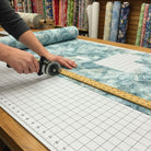 Carmon's Quilt Shop employee using a rotary cutter to trim teal and white marble pattern Smooth Sailing quilt fabric