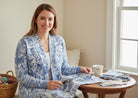 Carmon's Quilt Shop Mythic Forest blue floral cotton fabric shown as a cardigan worn by a woman at a wooden table.