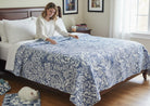 Woman sitting on a bed covered with Carmon's Quilt Shop Mythic Forest blue floral and animal print cotton quilt fabric