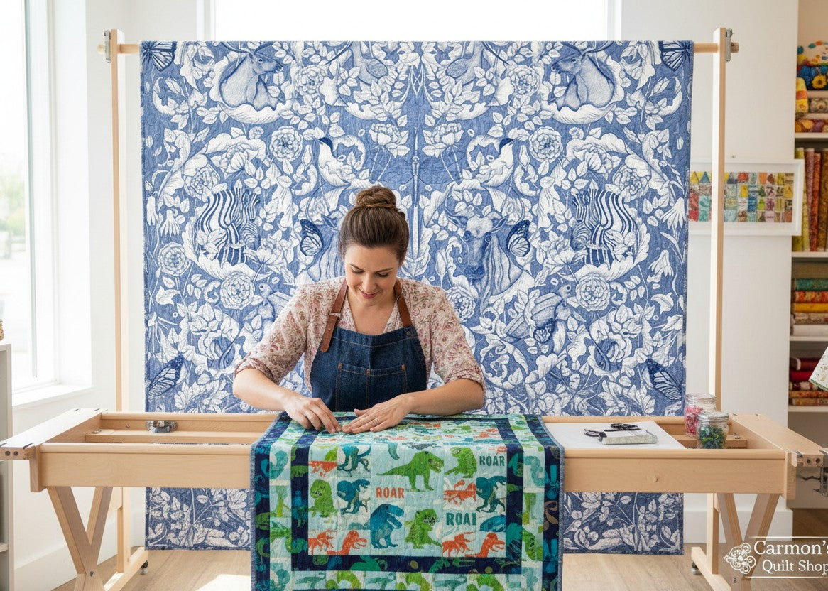 Carmon's Quilt Shop Mythic Forest blue cotton fabric with animal and floral print on a quilt frame with a quilter.