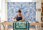 Carmon's Quilt Shop Mythic Forest blue cotton fabric with animal and floral print on a quilt frame with a quilter.