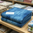 Carmon's Quilt Shop Panorama navy blue cotton fabric with abstract wood grain texture folded on a store shelf