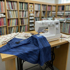 Carmon's Quilt Shop navy wood-textured cotton fabric being sewn on a machine in a fabric store setting.