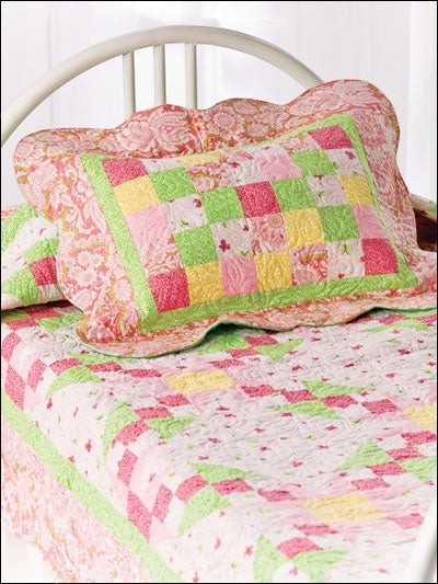 Carmon's Quilt Shop baby quilt featuring a pink, yellow, and green patchwork design with scalloped edges on a bed.