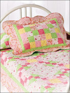 Carmon's Quilt Shop baby quilt featuring a pink, yellow, and green patchwork design with scalloped edges on a bed.
