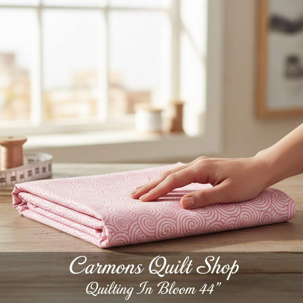 Carmon's Quilt Shop pink cotton fabric with a white daisy scroll swirl pattern, folded on a wooden table.