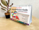 Carmon's Quilt Shop Quilter's Quick-Reference Guide with color-coded tabs and spiral binding on a wooden table.