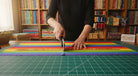 Carmon's Quilt Shop rainbow ombre cotton fabric being cut with a rotary cutter on a green cutting mat in a studio.