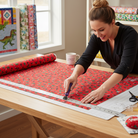 Carmon's Quilt Shop woman cutting red Coca-Cola Christmas logo toss cotton fabric with a rotary cutter on a table