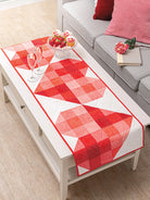 Carmon's Quilt Shop red and white geometric quilted table runner on a coffee table with strawberries and cupcakes.