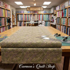 Carmon's Quilt Shop Meadow Breeze sage green floral 108-inch wide cotton quilt backing fabric on a cutting table.