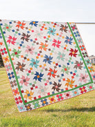 Carmon's Quilt Shop Scrap-Happy quilt featuring colorful pinwheel blocks and a green border hanging outdoors