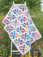 Carmon's Quilt Shop Scrap-Happy quilt featuring colorful geometric patterns on a white background in a garden setting.