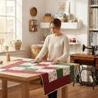 Woman sewing a festive quilt with Carmon's Quilt Shop Snowbound White Ornaments cotton fabric in a bright craft room.