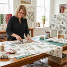 Carmon's Quilt Shop owner cutting Figo Snowbound white cotton fabric with festive holiday print on a wooden table