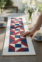 Carmon's Quilt Shop Stars & Ribbons table runner featuring red, white, and blue star blocks on a wooden table.