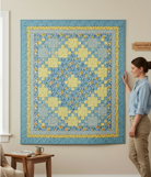Carmon's Quilt Shop Sunny Skies quilt kit featuring a blue and yellow floral patchwork design hanging on a wall.