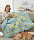 Woman sitting on a sofa with a blue and yellow Sunny Skies quilt kit from Carmon's Quilt Shop and a golden retriever