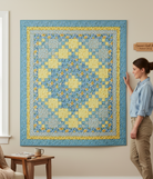 Carmon's Quilt Shop Sunny Skies quilt kit featuring a yellow and blue floral patchwork design hanging on a wall
