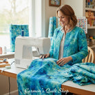 Carmon's Quilt Shop woman sewing a turquoise watercolor cotton quilt backing fabric on a machine in a bright studio.