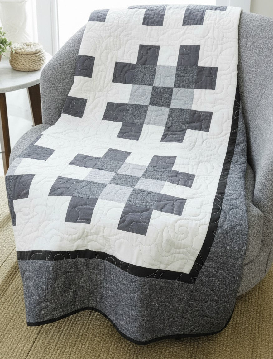 Carmon's Quilt Shop Annie's Quilting two-color quilt featuring a grey and white geometric pattern draped on a chair.
