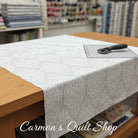 Carmon's Quilt Shop Light As Air white 100% cotton quilting fabric with elegant pattern on a wooden cutting table