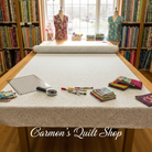 Carmon's Quilt Shop white Robert Kaufman Light As Air cotton fabric spread on a cutting table with quilting tools.