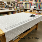 Carmon's Quilt Shop white Robert Kaufman Light As Air cotton fabric with snowflake pattern on a wooden cutting table.